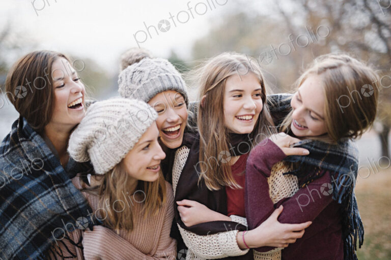 Five young people, girls, friends in warm shawls and woolly hats outdoors.