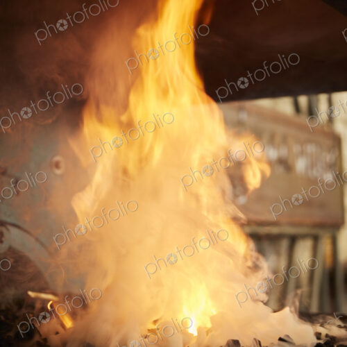 Flames and smoke billowing from a forge fire in a metal workshop.