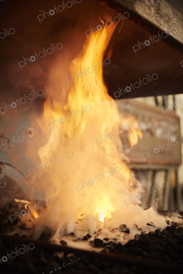 Flames and smoke billowing from a forge fire in a metal workshop.