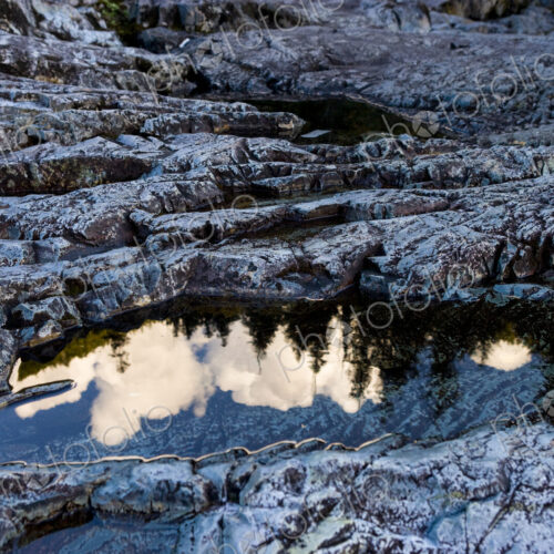 Forest scene and rocks on a hillside, the clouds and the tree line reflected in the… Forest scene and rocks on a hillside, the clouds and the tree line reflected in the…