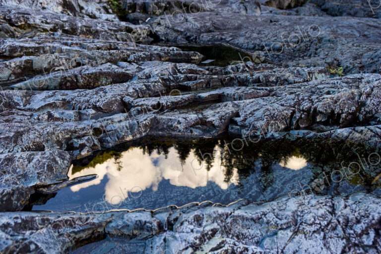 Forest scene and rocks on a hillside, the clouds and the tree line reflected in the…