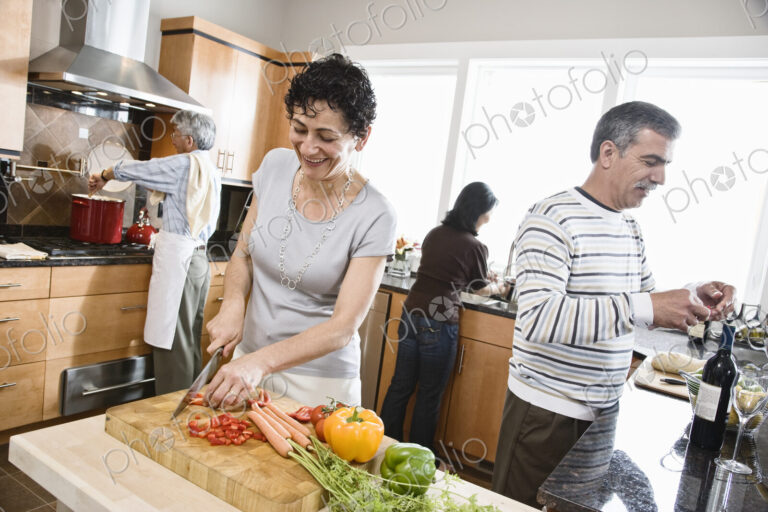 Four friends, two couples preparing a healthy meal, chopping vegetables in a kitchen,…