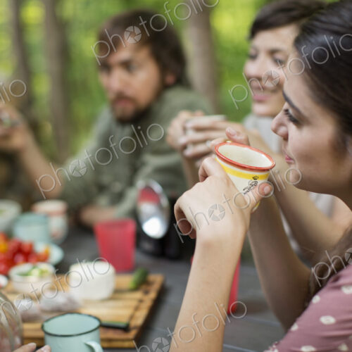 Four people seated around a wooden table outdoors in woodland sharing a meal. Four people seated around a wooden table outdoors in woodland sharing a meal.