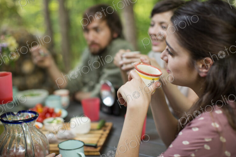 Four people seated around a wooden table outdoors in woodland sharing a meal.