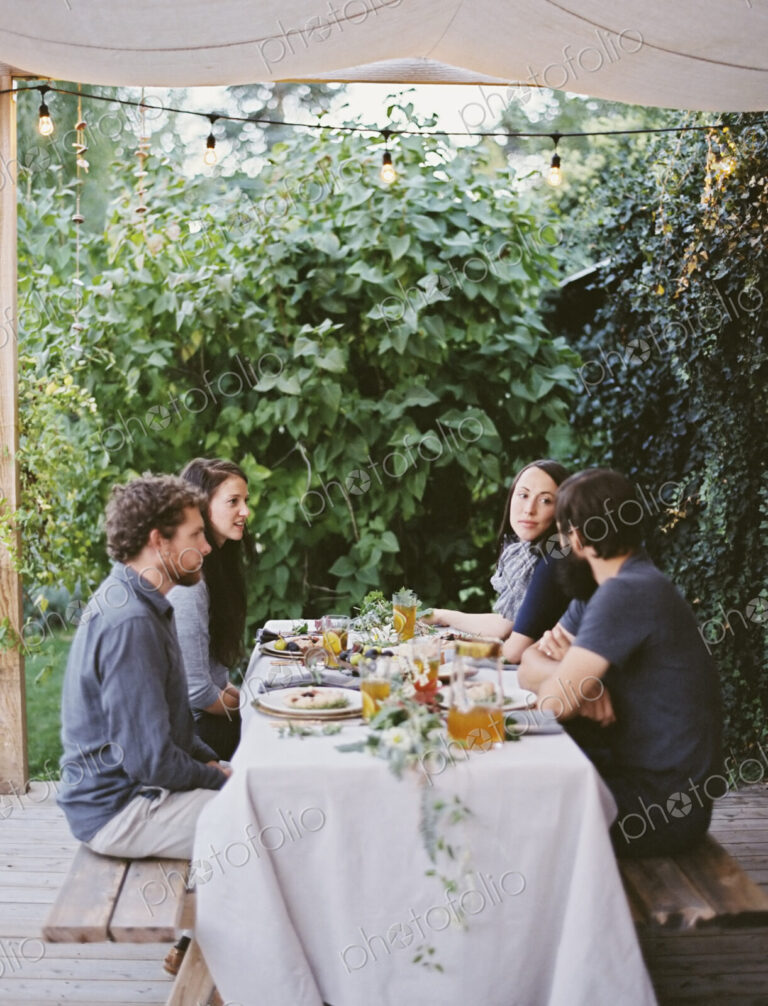 Four people seated at a table in the garden. Place settings and decorations on a white…