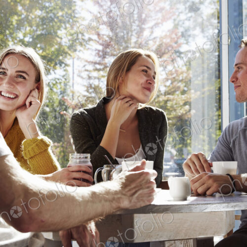 Four people sitting at a table talking, with mugs and jars of smoothies. Four people sitting at a table talking, with mugs and jars of smoothies.