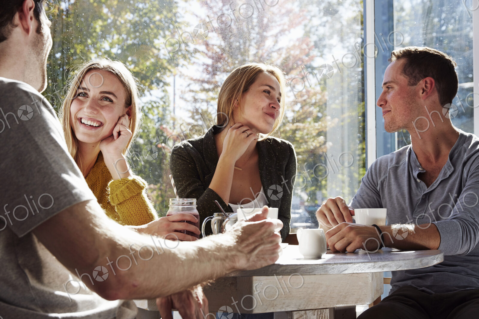 Four people sitting at a table talking, with mugs and jars of smoothies.