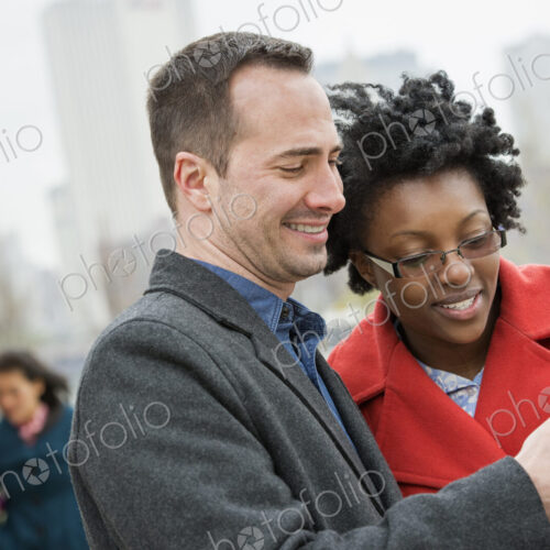 Four people, two in the background and two checking a phone. Four people, two in the background and two checking a phone.