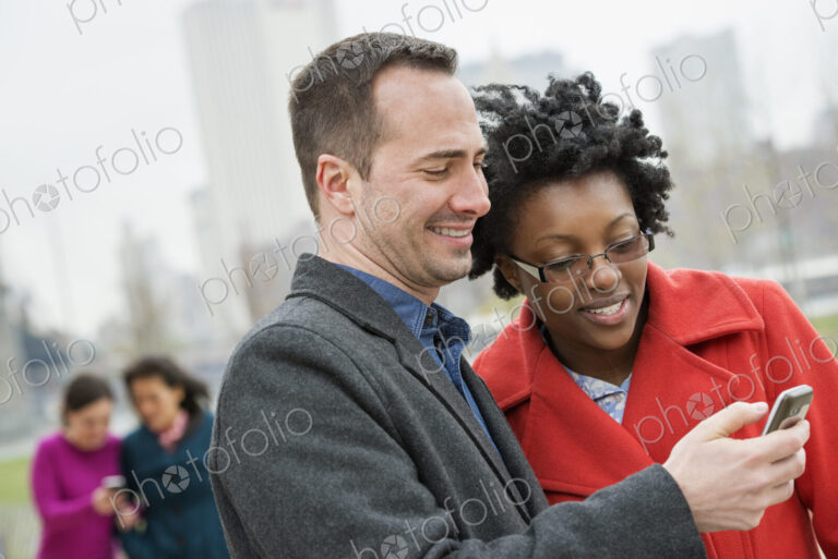 Four people, two in the background and two checking a phone.