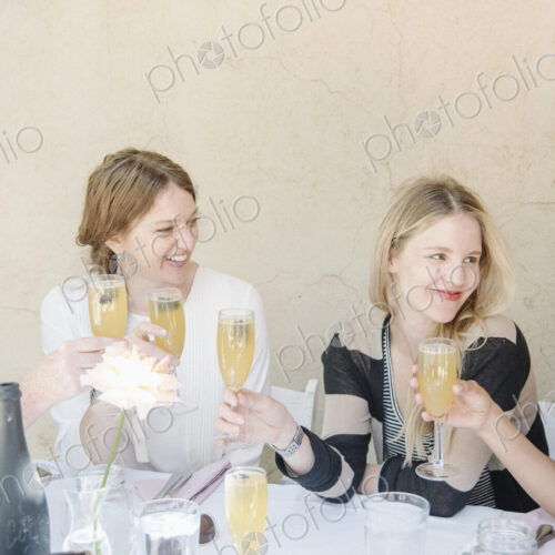 Four smiling women sitting at a table, holding glasses of champagne, toasting.