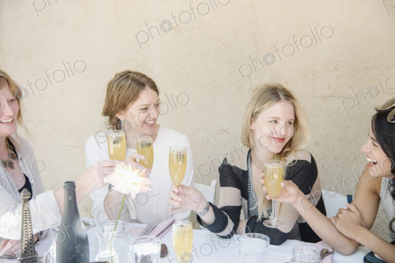 Four smiling women sitting at a table, holding glasses of champagne, toasting.