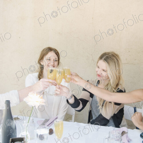 Four smiling women sitting at a table, holding glasses of champagne, toasting.