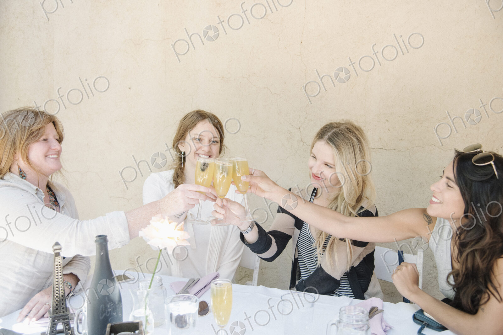 Four smiling women sitting at a table, holding glasses of champagne, toasting.