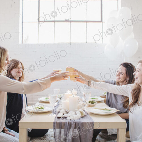 Four women seated at a low table, raising their glasses in a toast to each other.
