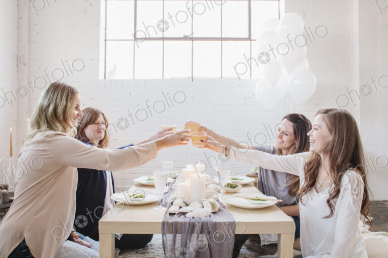 Four women seated at a low table, raising their glasses in a toast to each other.