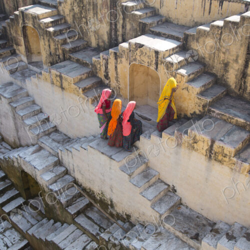 Four women wearing saris walking up stairwell around water pool