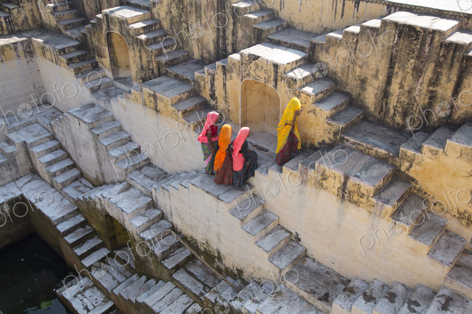 Four women wearing saris walking up stairwell around water pool