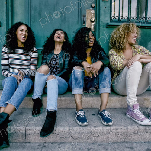 Four young women with curly hair sitting side by side on steps outside a building. Four young women with curly hair sitting side by side on steps outside a building.