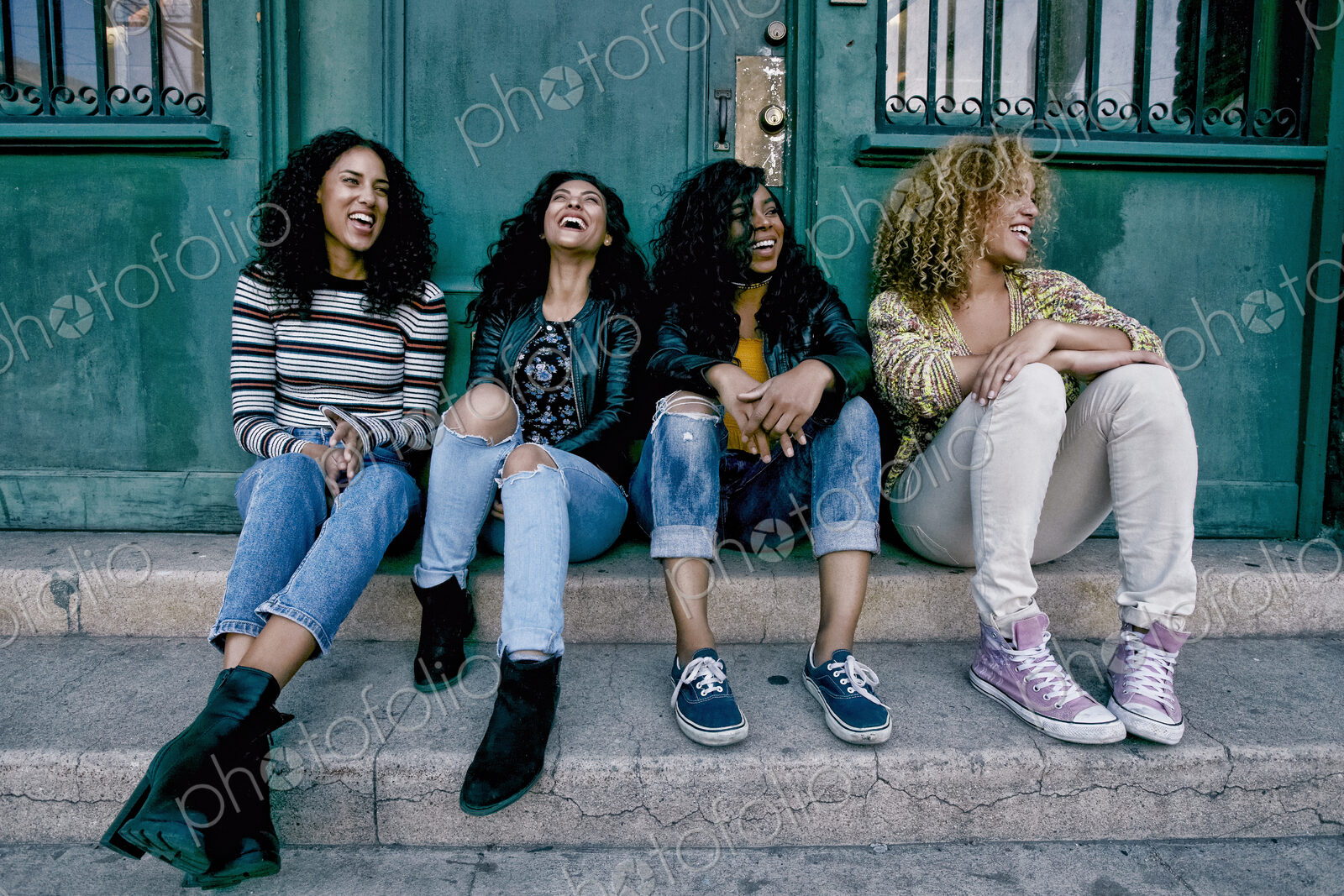 Four young women with curly hair sitting side by side on steps outside a building.