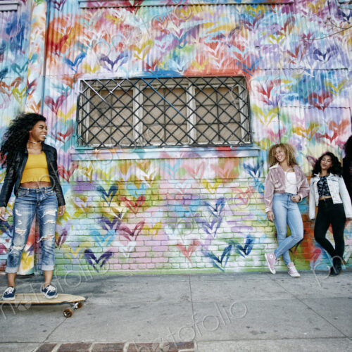 Four young women with curly hair standing in front of shutter covered in colourful… Four young women with curly hair standing in front of shutter covered in colourful…
