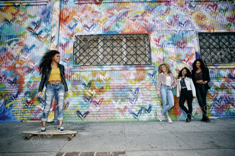 Four young women with curly hair standing in front of shutter covered in colourful…