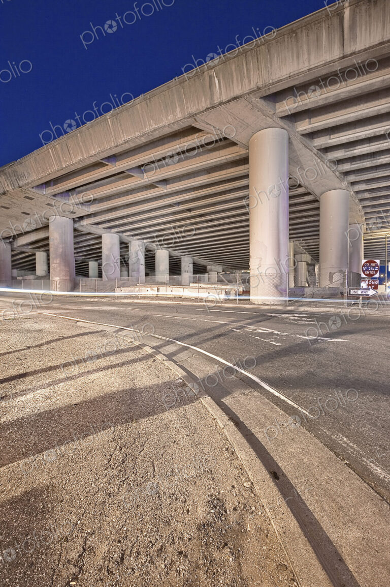 Freeway Overpass Support Structure casting shadows over a road at night.