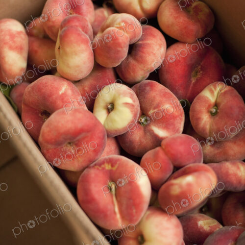 Fresh fruit on an organic farmstand. Doughnut peaches in a box.