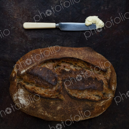 Freshly baked loaf of bread in an artisan bakery with a knife and portion of butter. Freshly baked loaf of bread in an artisan bakery with a knife and portion of butter.