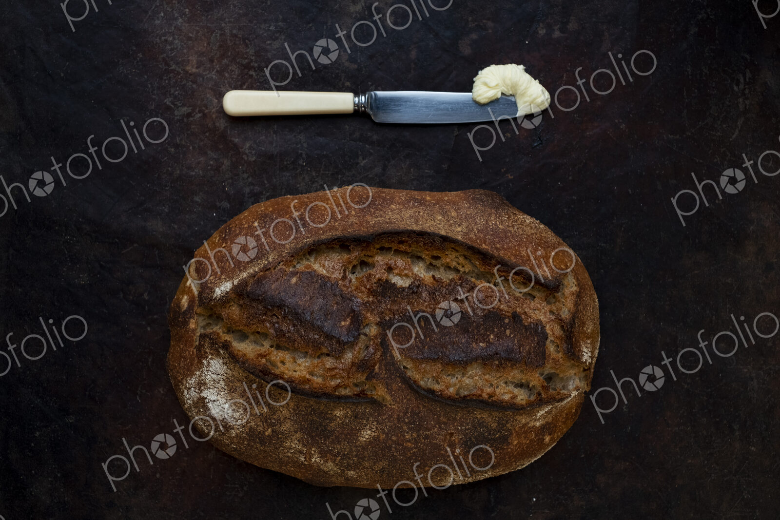 Freshly baked loaf of bread in an artisan bakery with a knife and portion of butter.