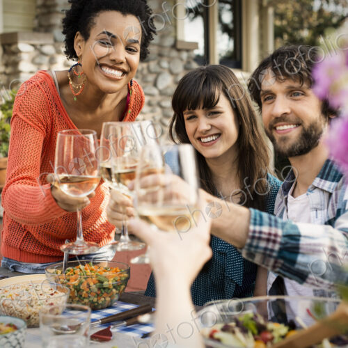 Friends around a table, men and women laughing and clinking wine glasses in a toast. Friends around a table, men and women laughing and clinking wine glasses in a toast.