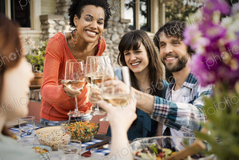 Friends around a table, men and women laughing and clinking wine glasses in a toast.