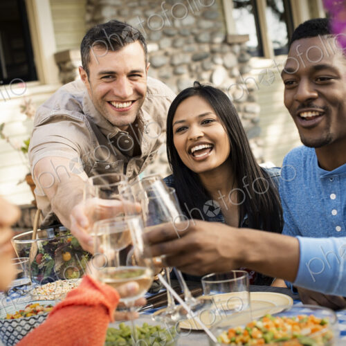 Friends around a table, men and women laughing and clinking wine glasses in a toast. Friends around a table, men and women laughing and clinking wine glasses in a toast.
