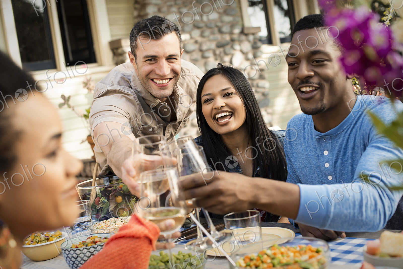 Friends around a table, men and women laughing and clinking wine glasses in a toast.