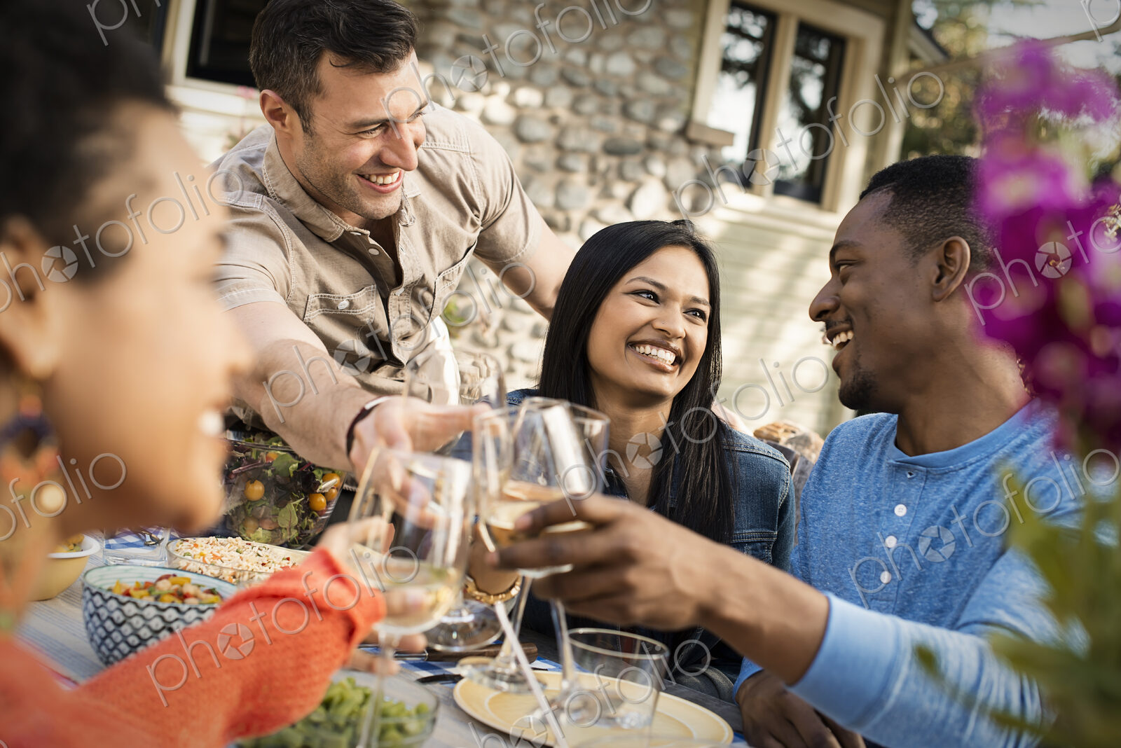 Friends around a table, men and women laughing and clinking wine glasses in a toast.