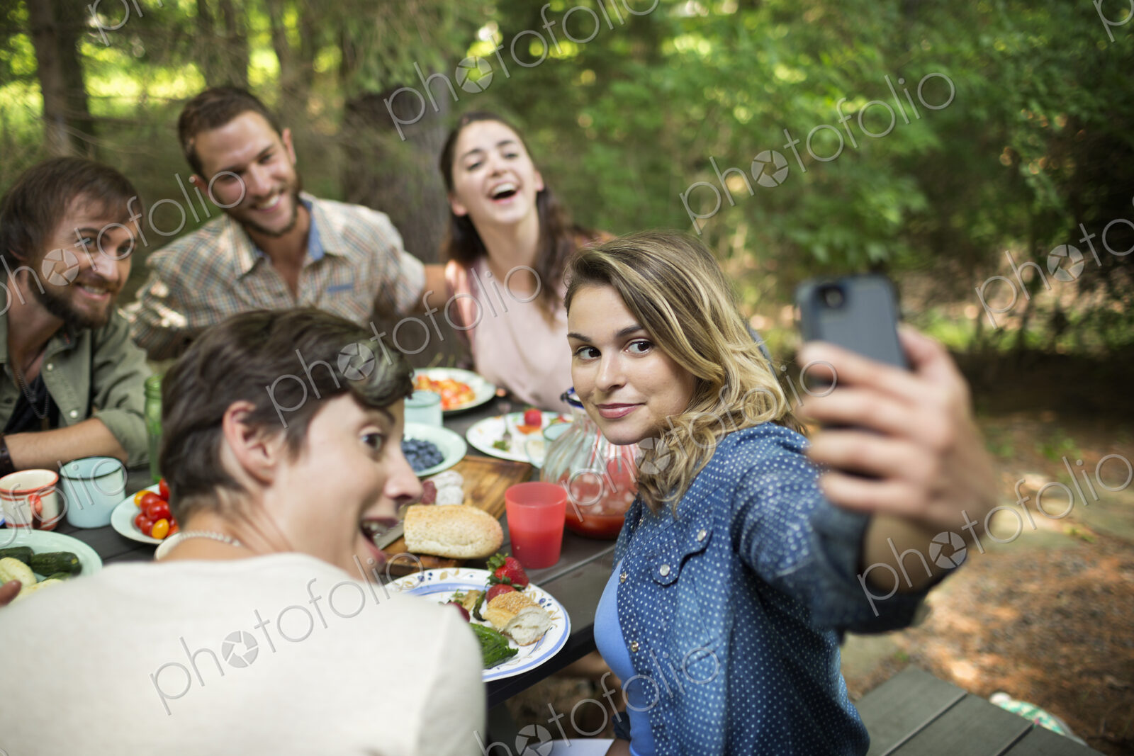 Friends at a woodland picnic, one woman taking a selfy of the group.