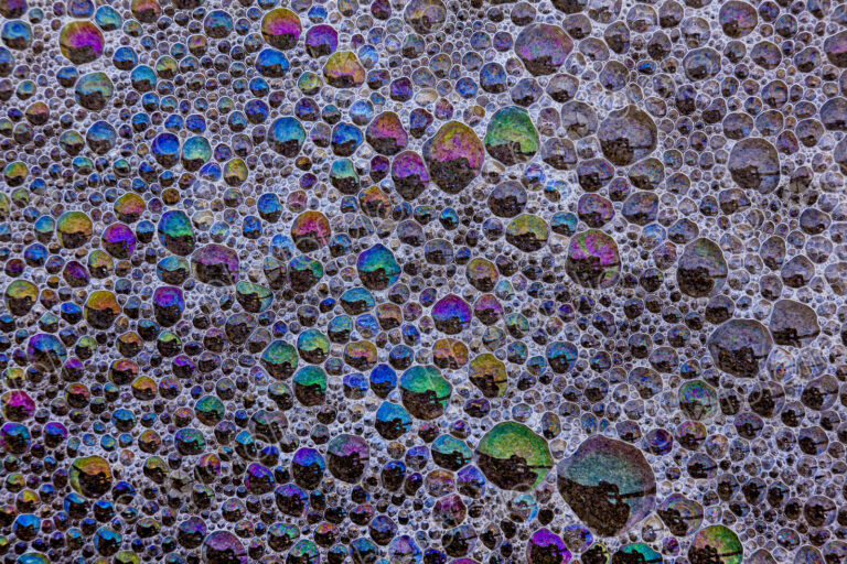 Froth and bubbles of air reflecting rainbow colours on the surface at Cannon Beach,…