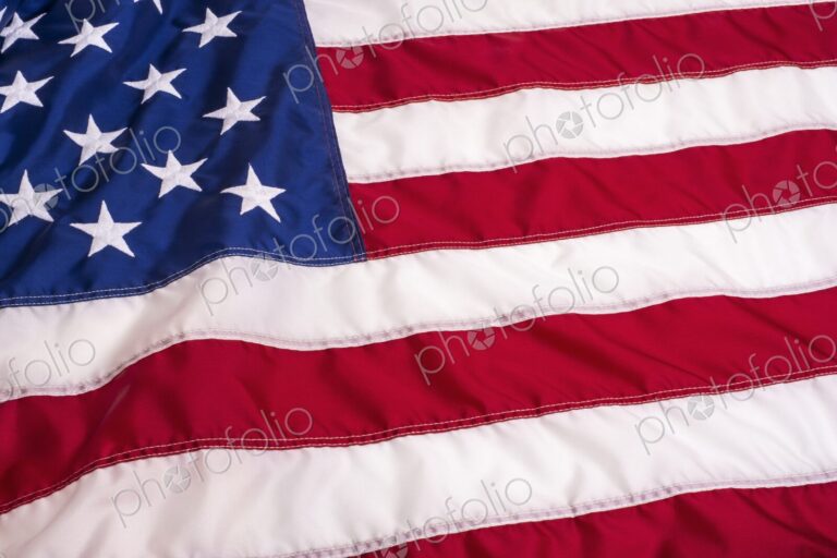 Full-frame close-up of the United States flag showing detailed stitching and texture -…