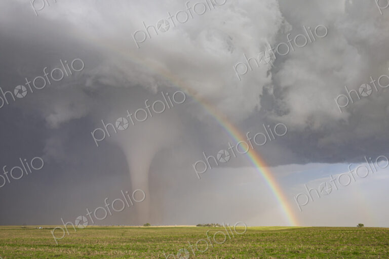 Fully Condensed Tornado with a Rainbow. a rotating column of air reaching the ground.