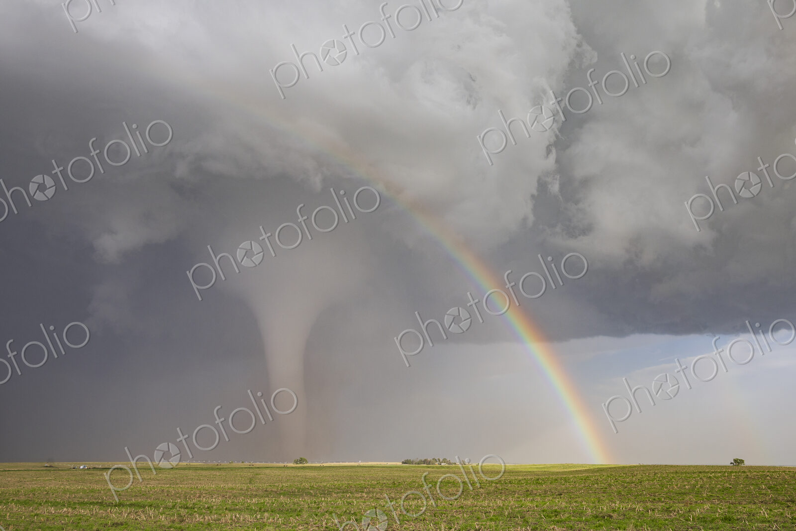 Fully Condensed Tornado with a Rainbow. a rotating column of air reaching the ground.
