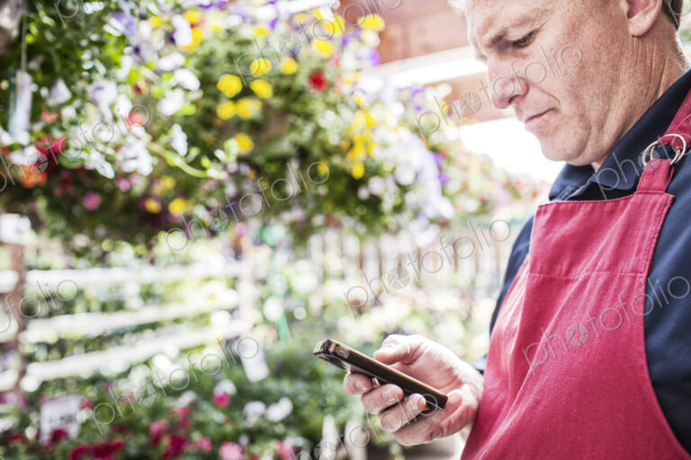 Garden center nursery caucasian male owner checking a note on his phone in the nursery.