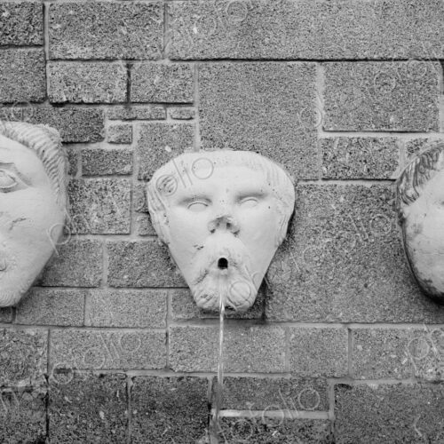 Gargoyle water fountain on stone wall.