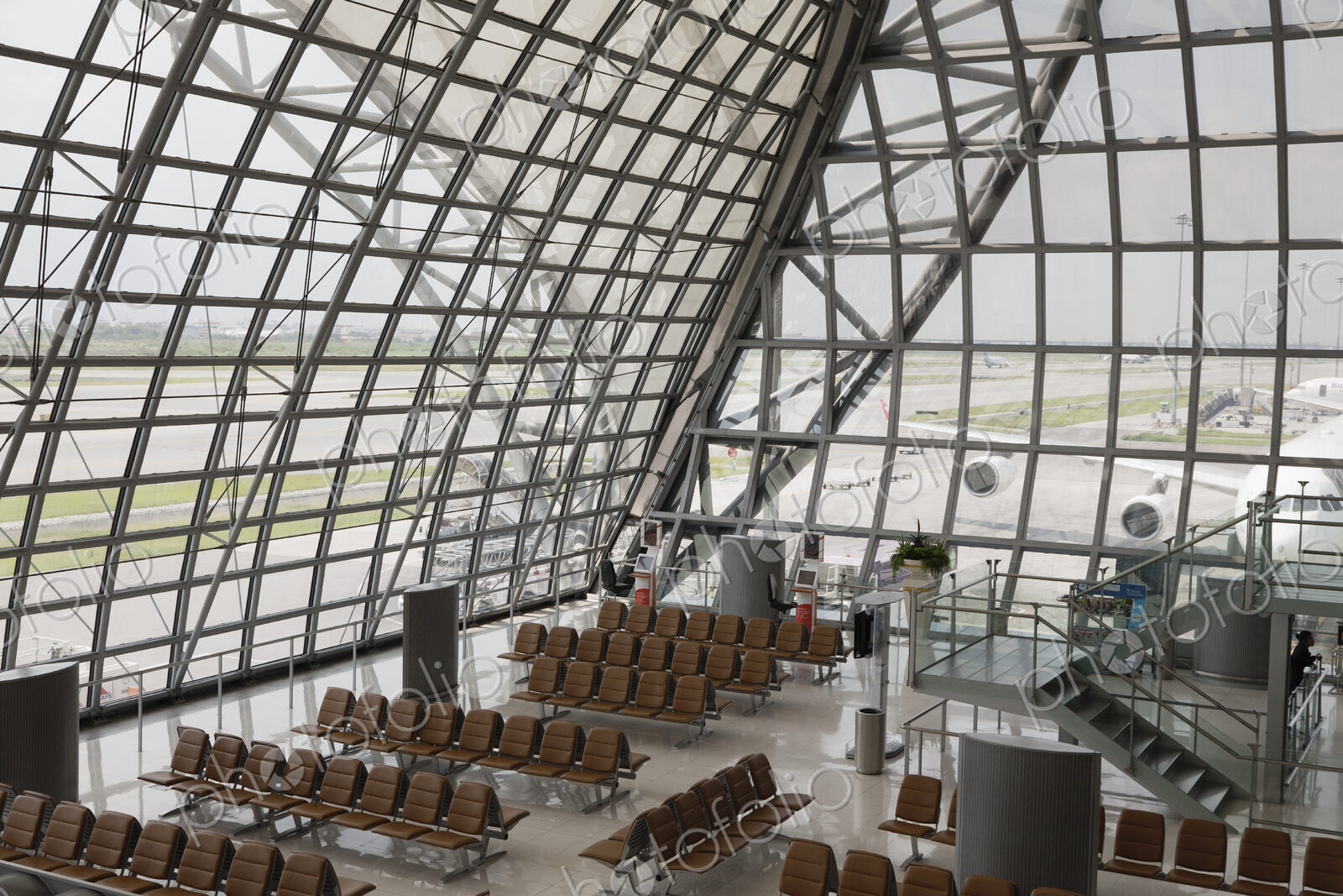 Gate and seats at Bangkok Airport with airplanes viewed through the glass walls.