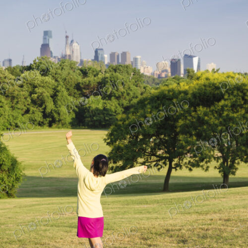 Girl dancing in park in front of city skyline.