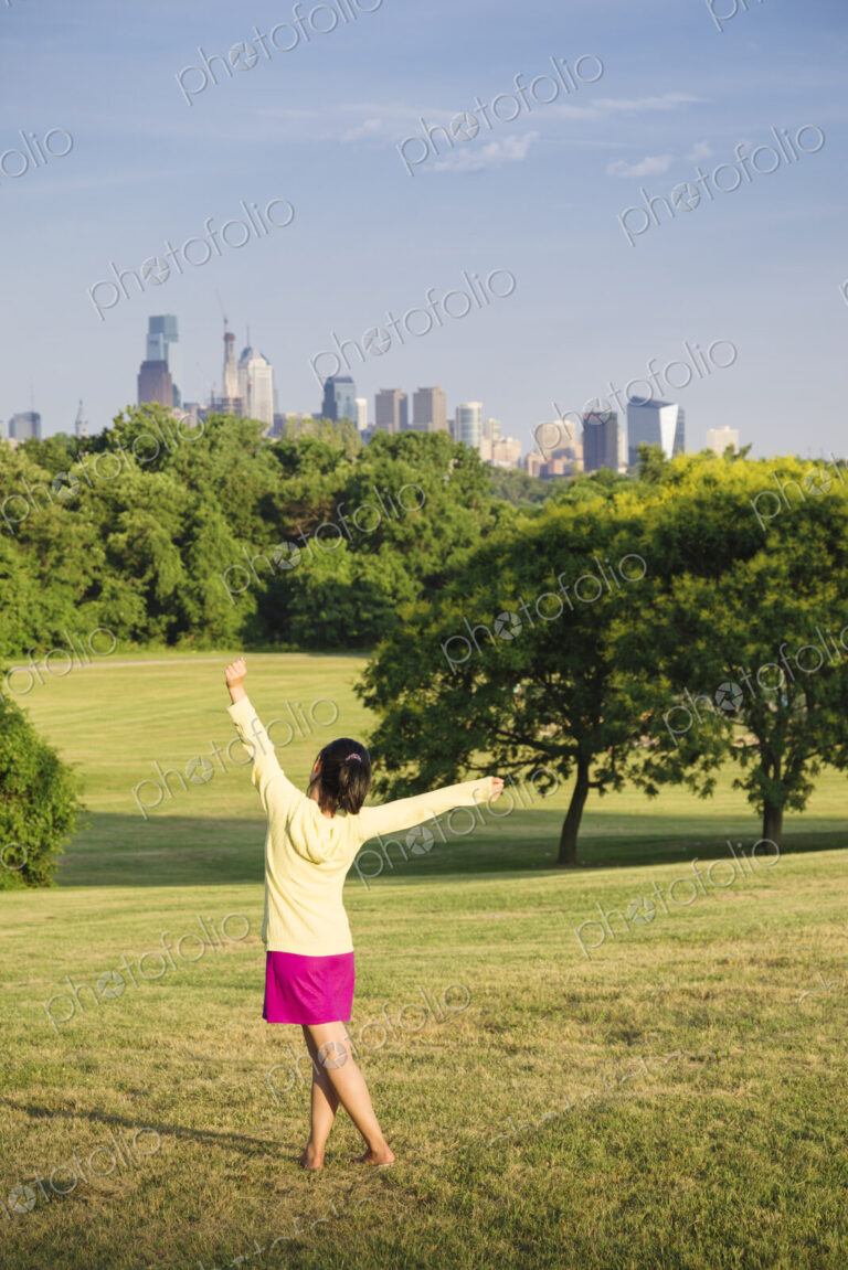 Girl dancing in park in front of city skyline.