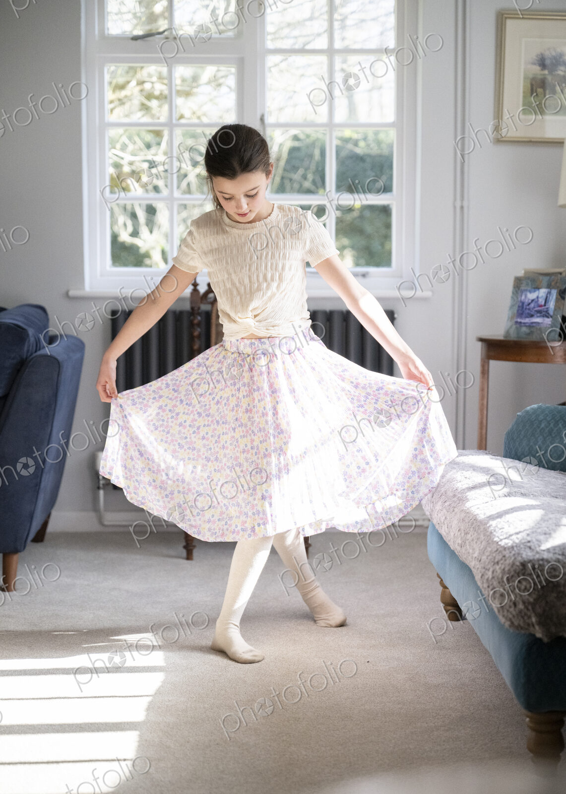 Girl facing camera curtseying in sitting room with head down.