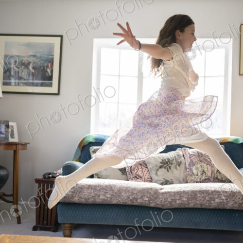 Girl leaping joyfully across sitting room with arms stretched out.