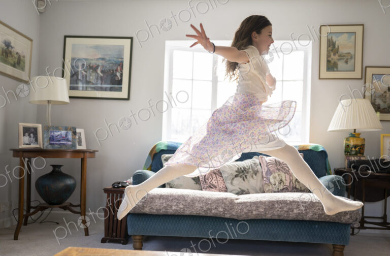 Girl leaping joyfully across sitting room with arms stretched out.