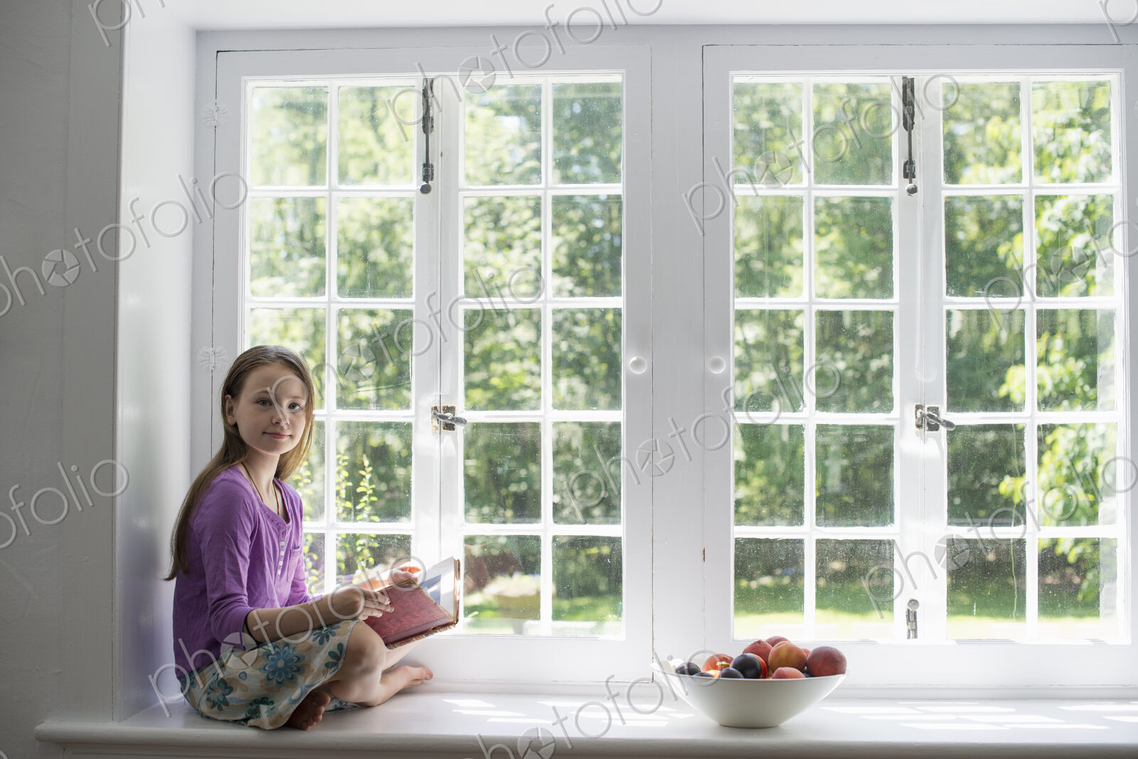 Girl sitting by a window, reading a book.