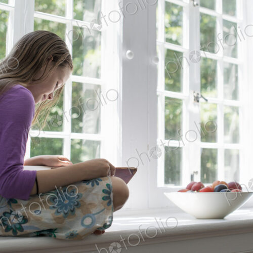 Girl sitting by a window, reading a book. Girl sitting by a window, reading a book.