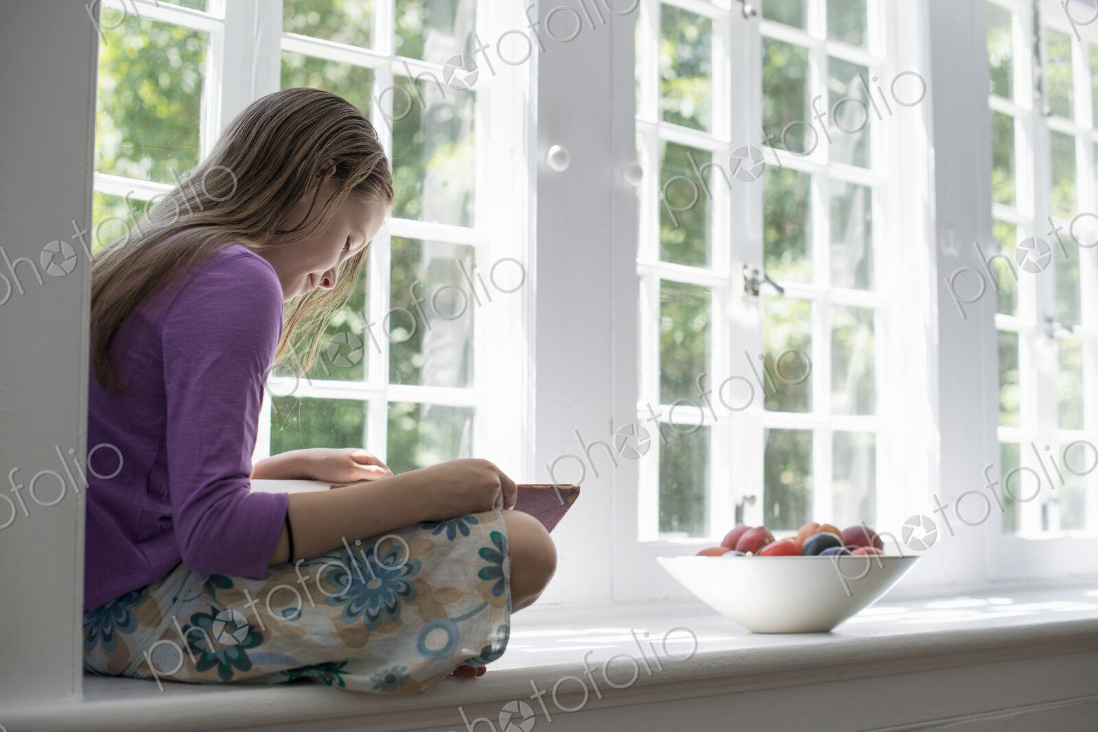 Girl sitting by a window, reading a book.